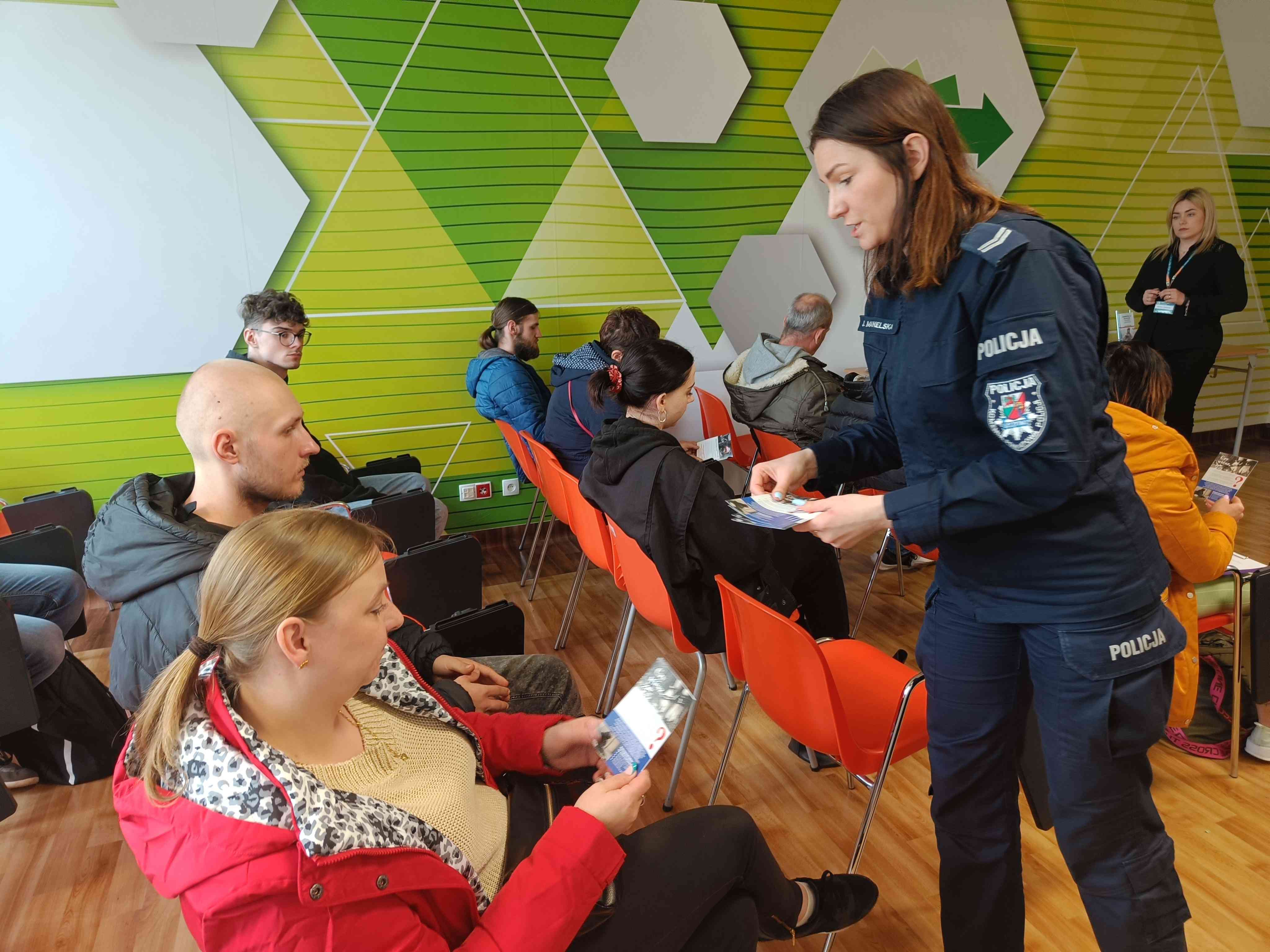 Policjanta na spotkaniu rozdająca broszury o rekrutacji w Policji wśród osób bezrobotnych